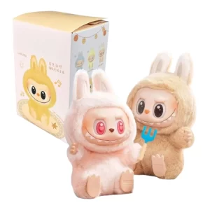 Plyšové figurky Labubu v kostýmech zajíčků, jedna růžová s červenýma očima a druhá béžová s vidličkou, vedle originální dárkové krabičky s ilustrací