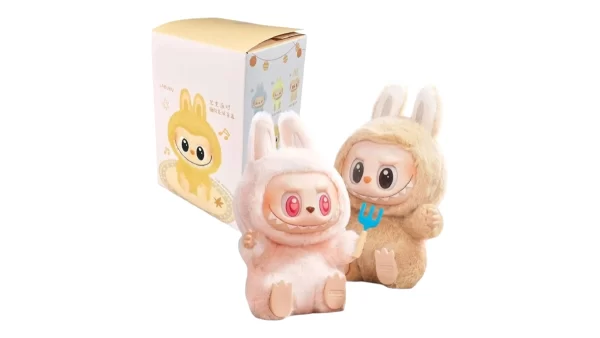 Plyšové figurky Labubu v kostýmech zajíčků, jedna růžová s červenýma očima a druhá béžová s vidličkou, vedle originální dárkové krabičky s ilustrací